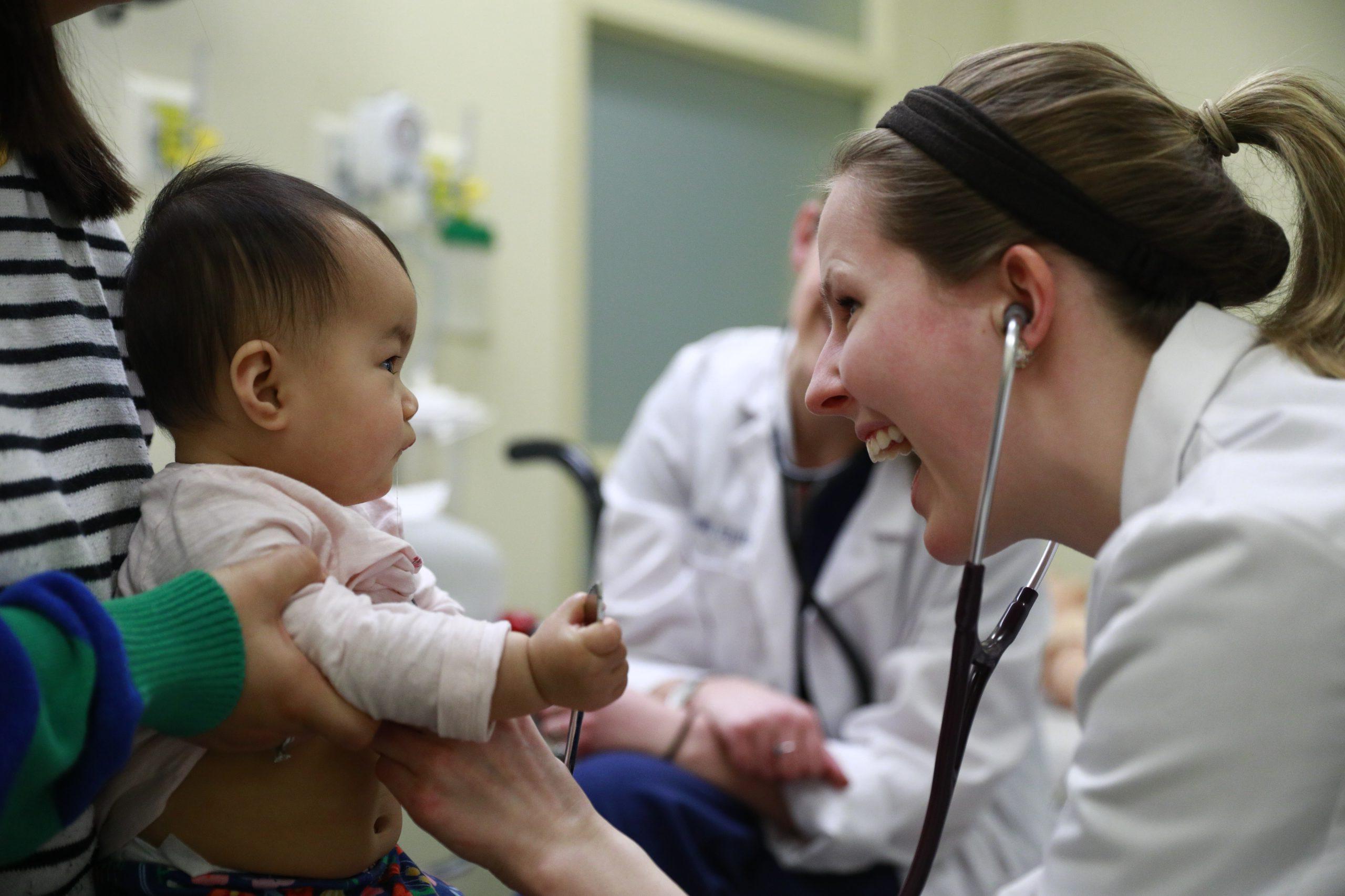 A pediatric student using a stethoscope on a young baby